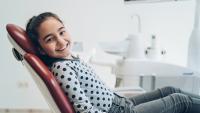 Girl sitting in dentist chair, smiling and happy